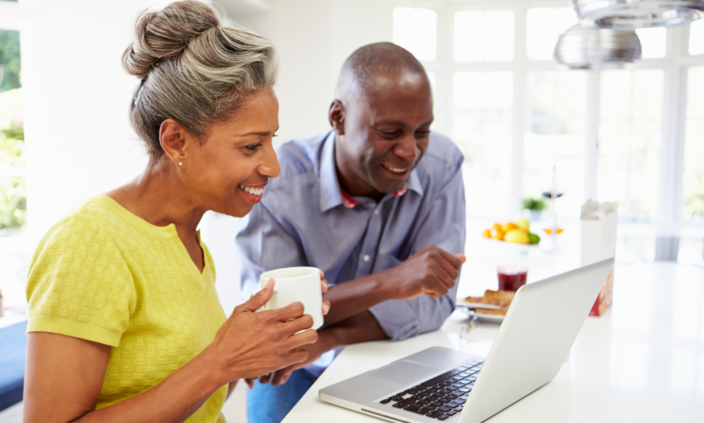 Older black couple looking at a laptop in their kitchen
